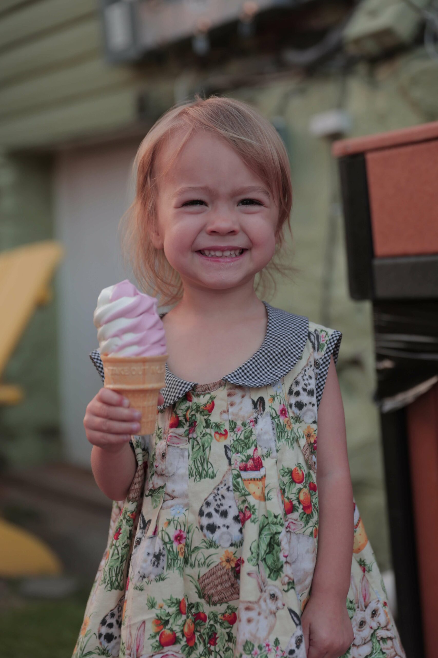 A young girl in a green dress smiles for the camera while holding a vanilla and raspberry swirl in a cone from Gruto's