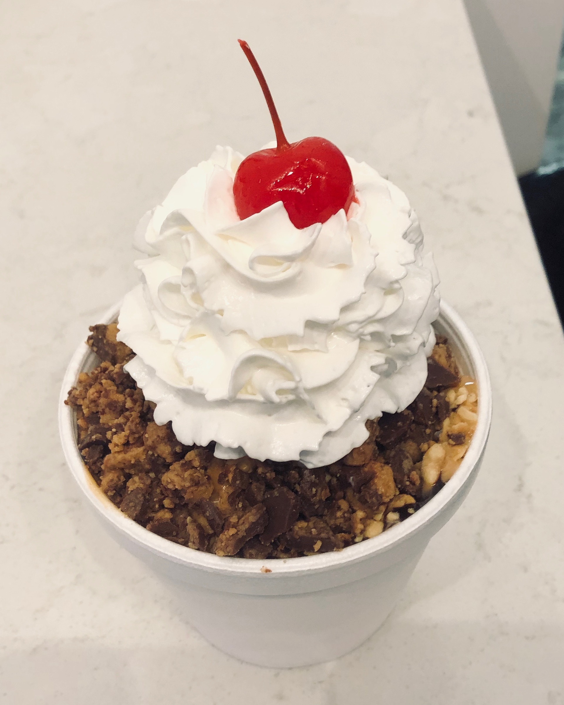 A Nutty Buddy from Gruto's in a white cup with whipped cream and a cherry on top